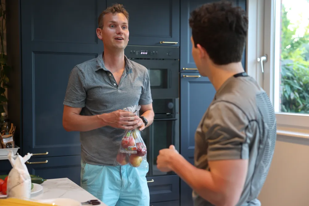 Twee mannen in gesprek in de keuken, één met een zak boodschappen