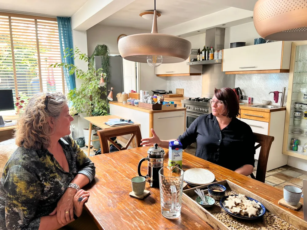 Twee vrouwen in gesprek aan de keukentafel met koffie