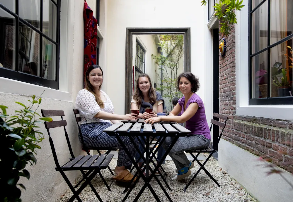 Drie vrouwen aan een tafeltje in een stadstuin lachen naar de camera