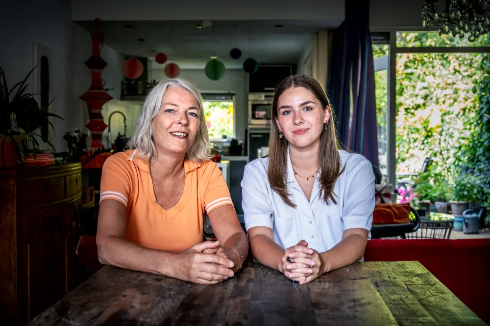 Een hospita en een student zitten samen aan tafel en kijken naar de camera